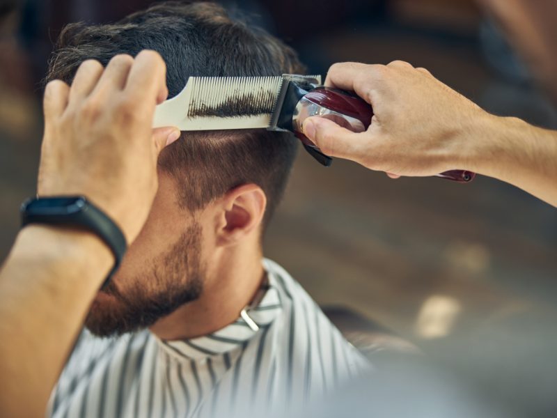 Barbier aan het werk bij een klant met gestreepte kapmantel